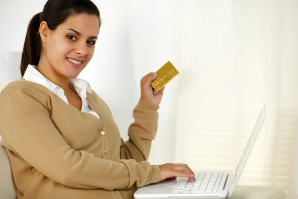 Mujer joven sosteniendo una tarjeta de crédito de oro con el ordenador portátil —  Fotos de Stock