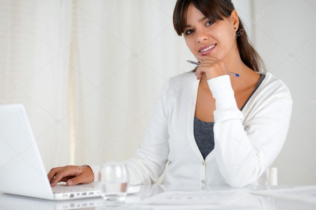 Smiling young woman looking at you using laptop