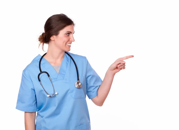 Encantadora enfermeira sorrindo e apontando para a esquerda — Fotografia de Stock