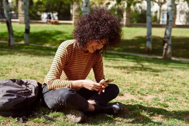 Gün boyunca parkta tek başına otururken gülümseyerek kısa mesaj okuyan sevimli siyah kadın.