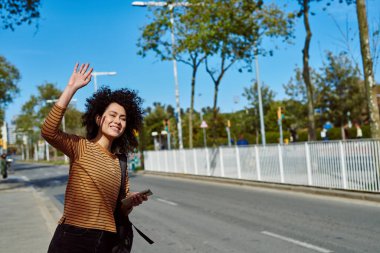 Neşeli genç siyahi kadın, gün boyunca yol kenarında sırt çantası ve cep telefonuyla taksi çağırıyordu.