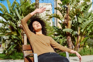 Gün boyunca dışarıda bir sandalyede dinlenirken yüzünü güneşten koruyan sevimli siyahi kadın.