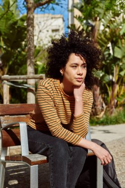 Dışarıda bir sandalyede tek başına otururken düşünceli görünen genç, tatlı siyahi kadın.