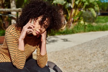 Gün boyunca dışarıda bir sandalyede tek başına otururken telefonla konuşan sevimli siyahi bir kadın.