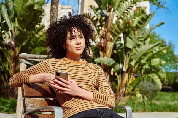 Attractive Young Black Woman Sitting Thoughtfully While Holding Smartphone Outdoors — Stock Photo, Image