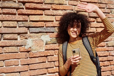 Gün içinde elinde cep telefonuyla güneşi engelleyen sevimli, genç siyah bir kadın.