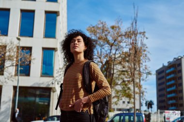 Sırt çantalı hoş, genç siyahi bir kadın gün boyunca şehirde tek başına duruyor.