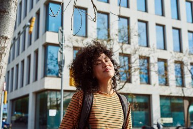 Sırt çantalı güzel siyah bir kadın. Gün boyunca gözleri kapalı şehirde duruyor.