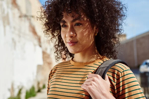 Beautiful young black woman walking alone with a backpack outdoors during the day