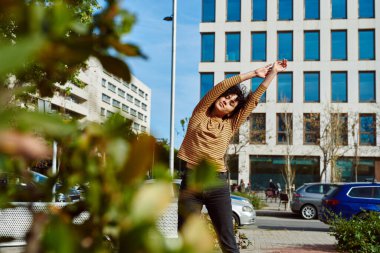 Genç, zinde, siyah bir kadın gün boyunca şehir dışında dikilirken gözlerini kapatarak kollarını uzatıyor.