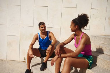 Genç ve zinde bir çift, spor yapmaya ara verip dışarıda merdivenlerde otururken sohbet ediyorlar.
