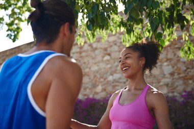 Spor yapan genç bir çift ağaçların altında dikilirken neşeli bir sohbet ediyorlar.