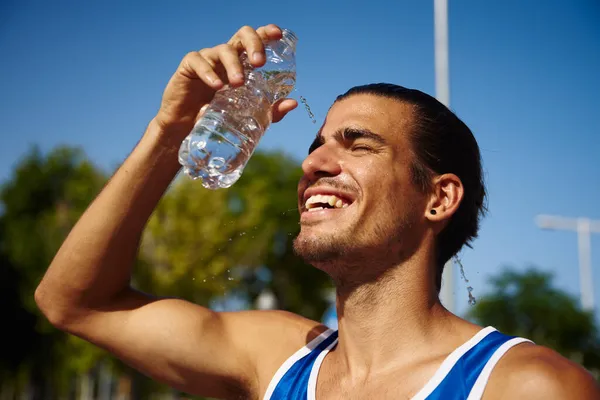 日中は屋外で顔に水を注ぎながら 陽気に笑顔を浮かべているスポーティ若い男 — ストック写真