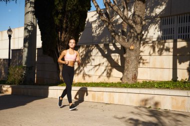Güneşli bir günde spor yaparken sokakta koşan güzel bir kadın.
