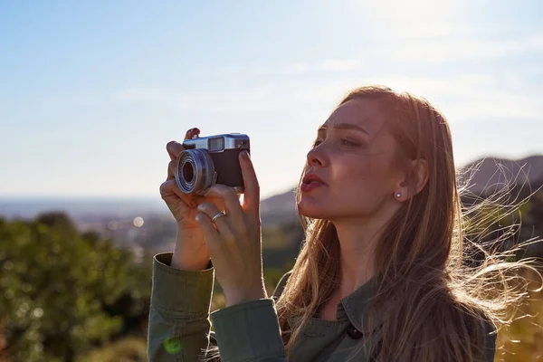 Woman holding camera and photographing mountains in sunset