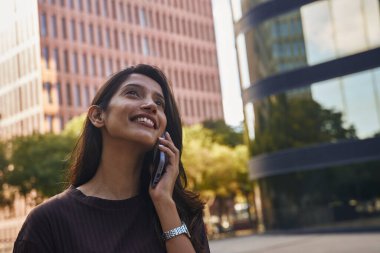 Güzel genç iş kadını sokakta cep telefonuyla konuşuyor.