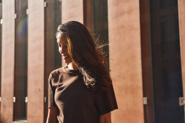 Saçları dağınık, genç ve güzel bir iş kadını. Sokakta durup gülümsüyor.