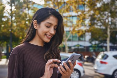 Cep telefonlu güzel bir iş kadını sokakta ayakta duruyor ve çalışıyor.