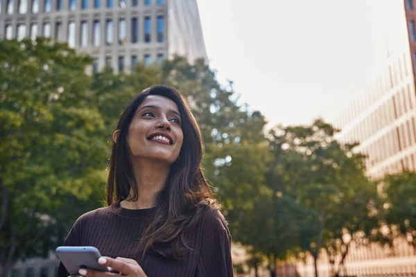 Smiling businesswoman standing on street with mobile phone