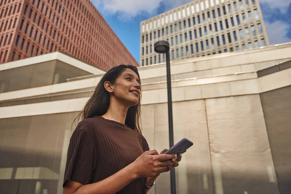 Young smart businesswoman with mobile phone looking away on street