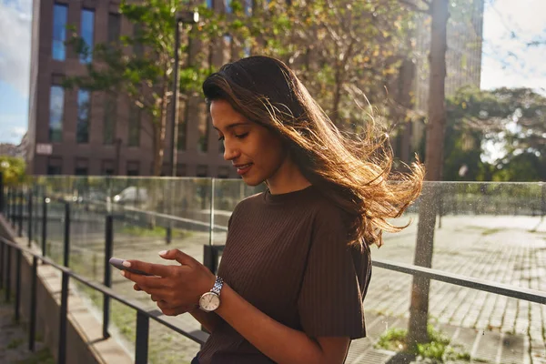 Parmaklıklara Yaslanmış Cep Telefonuyla Güneşli Caddede Duran Genç Bir Kadını — Stok fotoğraf