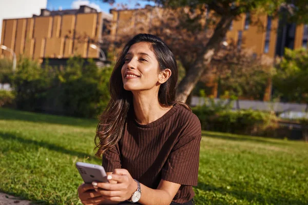 Gülümseyen Genç Kadını Parkta Cep Telefonuyla Oturuyor Çalışıyor — Stok fotoğraf