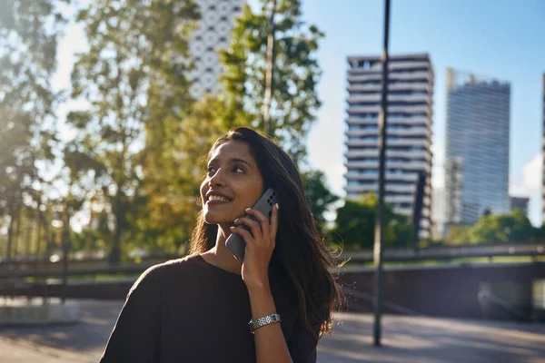 Young laughing businesswoman laughing happily while talking by mobile phone on city street