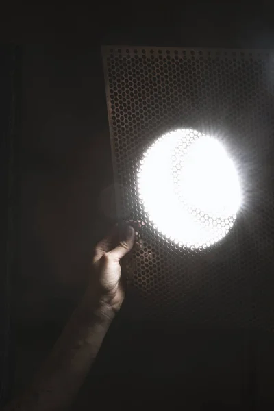 Människans Hand Håller Metallplåt Med Cirkulära Hål Framför Ljuset För — Stockfoto