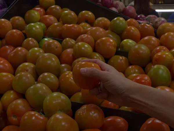 Süpermarkette bir sürü taze domates arasından olgun domatesleri seçen bir adam.