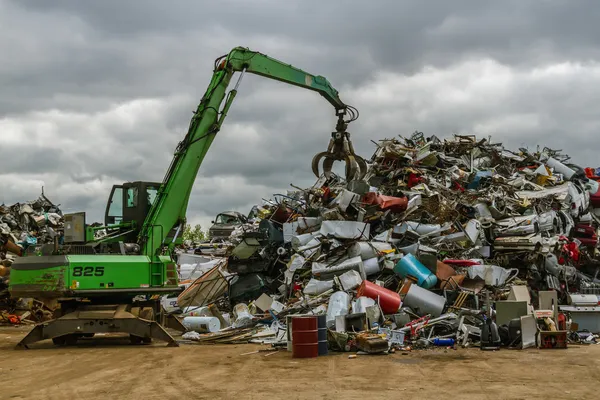 Zelené hydraulických zařízení, které pracuje v šrotiště plná různých objektů — Stock fotografie