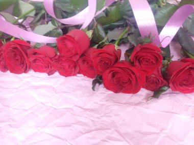 On a pink background, a bouquet of red roses, and a plate for the inscription