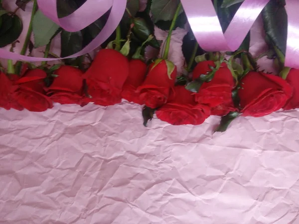 On a pink background, a bouquet of red roses, and a plate for the inscription