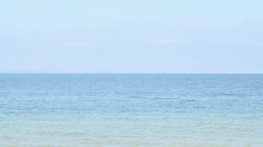 Sakin mavi deniz okyanusu, sahilde ufuk, açık gökyüzü ve beyaz kum arka planı. Güzel doğa ve manzara konsepti. 4K video görüntüleri