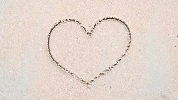白い砂浜のビーチの背景にある海と波によるハート型の手描きの拭き取りと使いやすさ 情熱と愛情の概念 自然景観とバレンタインデーのコンセプト 4Kフッテージビデオ — ストック動画