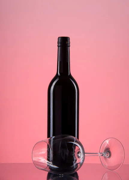 Flasche mit Rotwein und Glas auf rotem Gefälle — Stockfoto