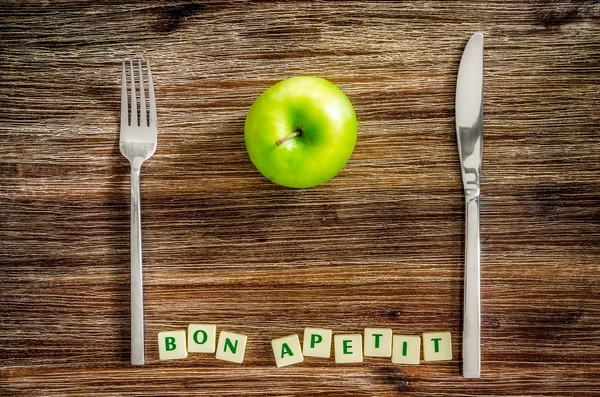 Silverbestick och apple på träbord med bon apetit tecken — Stock fotografie