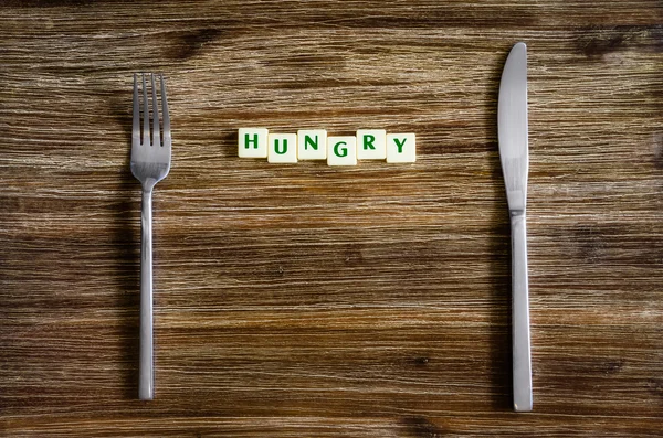 Příbory sada na dřevěný stůl s znamení hlad — Stock fotografie
