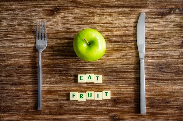 Silverware and apple on wooden table with sign Eat fruit — Stock Photo, Image