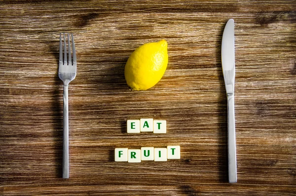 Silverware and lemon on wooden table with sign Eat fruit — Stock Photo, Image
