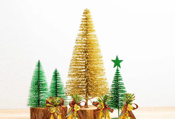 Gold Christmas trees and green Christmas trees with gold bells on the table and white background. Front view, copy space.