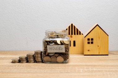 İçinde para yığını olan cam bir kavanozda para ve finansal konsept için fotokopi alanı olan kahverengi ahşap evler.