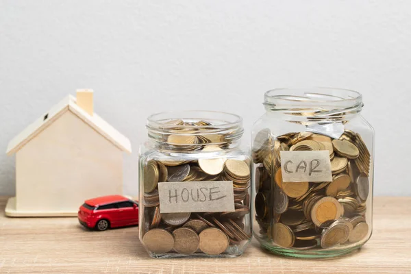 テーブルの上にお金と木の家と赤い車を節約するためのガラス瓶のコイン 金融概念 — ストック写真