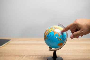 Dünya modeli üzerindeki el noktası kahverengi masanın üzerinde beyaz arkaplan fotokopi alanı ile dünya haritasını aramak için duruyor.