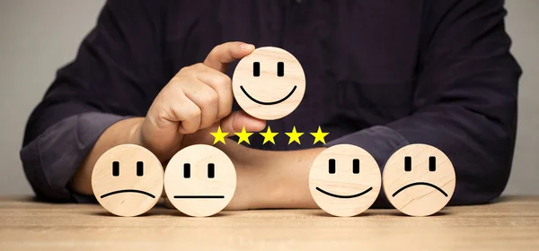 The concept of rating the highest level of service satisfaction. Positive opinion poll Man holding a smile face wooden block rated 5 stars. Customer service best excellent.