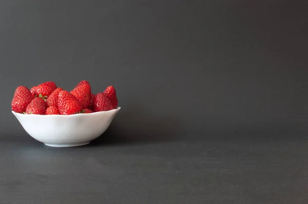 Strawberries, natural and sweet ripe strawberries in white bowl with copy space on right. Isolated on dark background, selective focus.