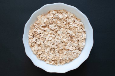 Yulaf ezmesi, organik ve vejetaryen yulaf ezmesinin beyaz bardakta üst görüntüsü. Popüler sağlıklı yulaf ezmesi koyu arka planda izole edilmiş, seçici odaklı.