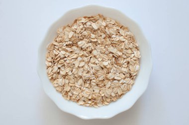 Doğal yulaf lapaları, beyaz kasedeki sağlıklı ve besleyici yulaf gevreklerinin üst görüntüsü. Beyaz arka planda izole edilmiş popüler mısır gevreği, seçici odaklanma.