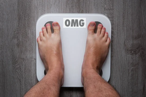 Üzerinde dengesi yazan akıllı terazilerin üzerinde duran yalınayak bir adamın en üst görüntüsü. Aman Tanrım. Gri ahşap zeminde duran boş dengeli beyaz ağırlıklar.