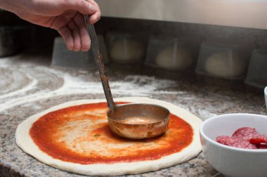 Erkek şef baharatlı kırmızı sos pizzası sürer. Çiğ hamur preformu. Pizza üretimi ve teslimatı.