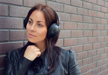 Siyah deri ceketli güzel bir kız telefonundan dış kulaklıklardan müzik dinliyor. Tuğla duvar Sokakta. Müzikle karmaşıklaşıyor. Yeni albüm.